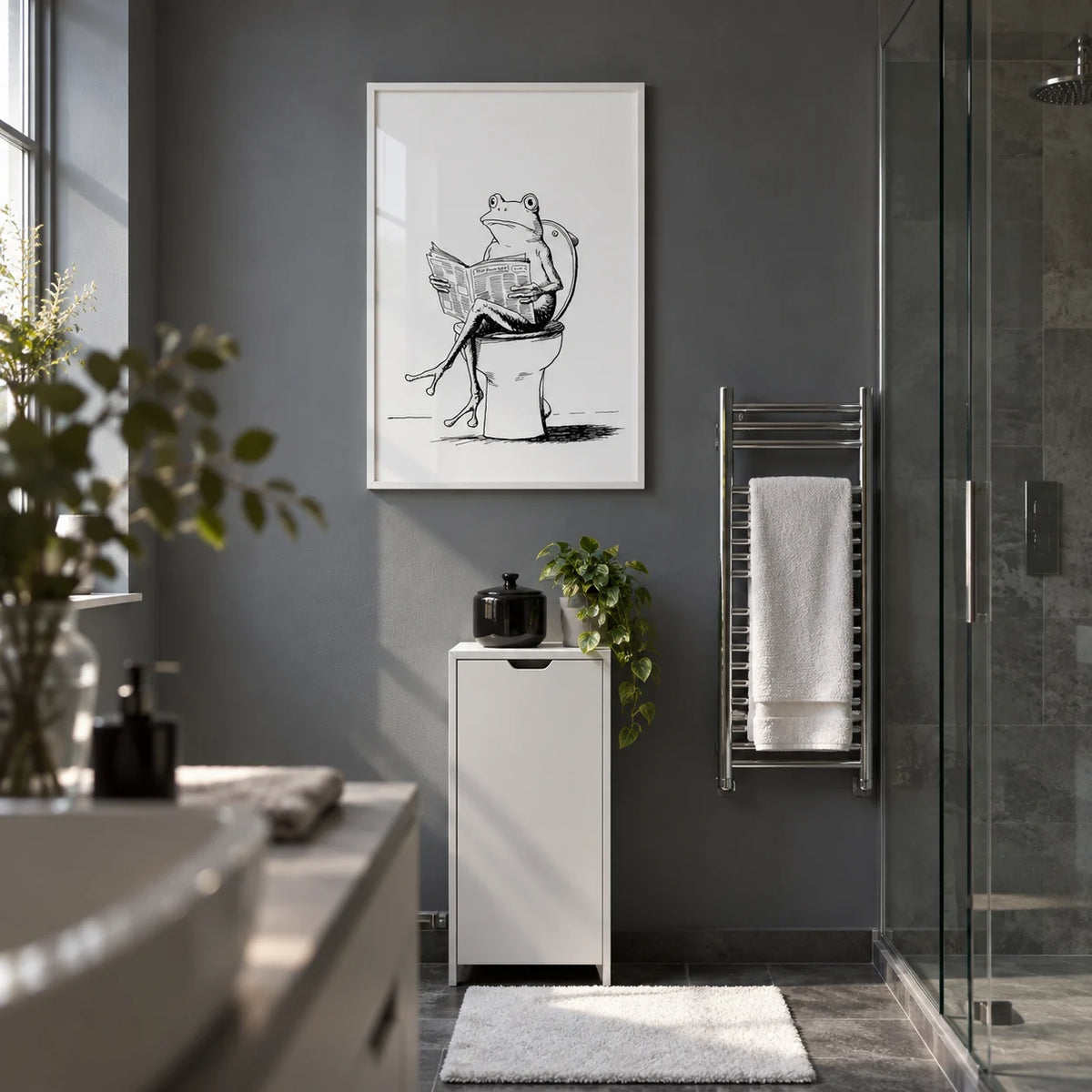 Cartoon Frog Wall Art, framed on the wall of a compact modern ensuite with a slate grey painted dry wall and a clear glass shower enclosure to one side in a bathroom