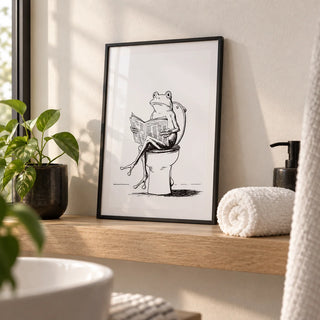 Cartoon Frog Wall Art, a small A4 framed print leaning on a pale oak shelf in a bathroom