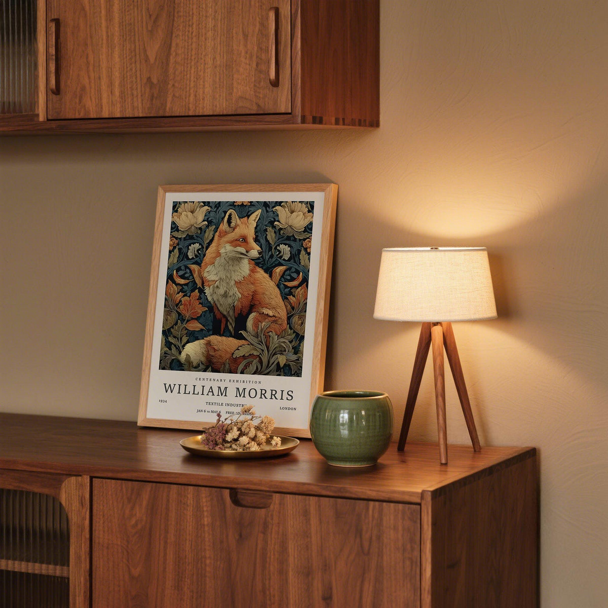 Print leaning on a wooden sideboard of a red fox surrounded by botanical elements with a lamp beside it