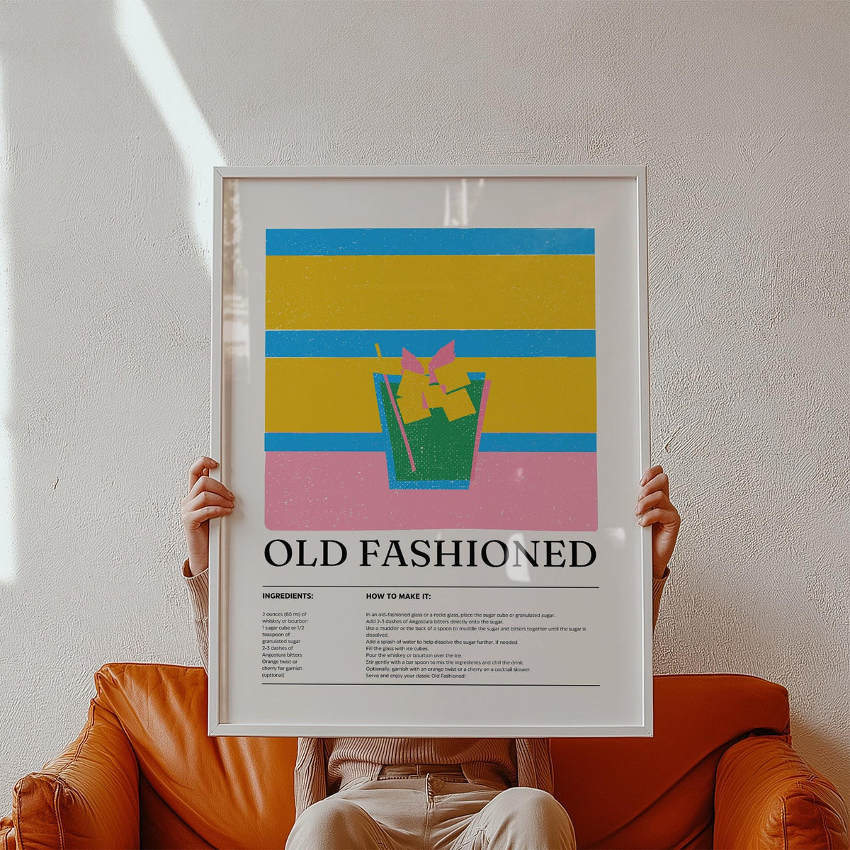 Framed print of Old Fashioned cocktail illustration with bold colours held by person on orange sofa