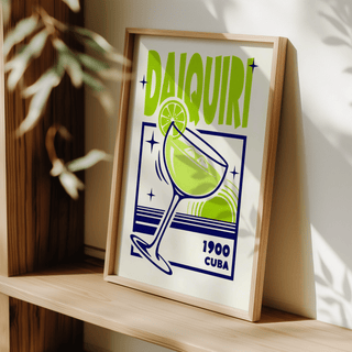 Framed Daiquiri art print with green and navy minimalist style leaning on a shelf near plant shadows