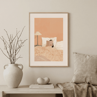 Woman Reading Book Art framed print with peach and cream tones above a wooden sideboard with a beige vase