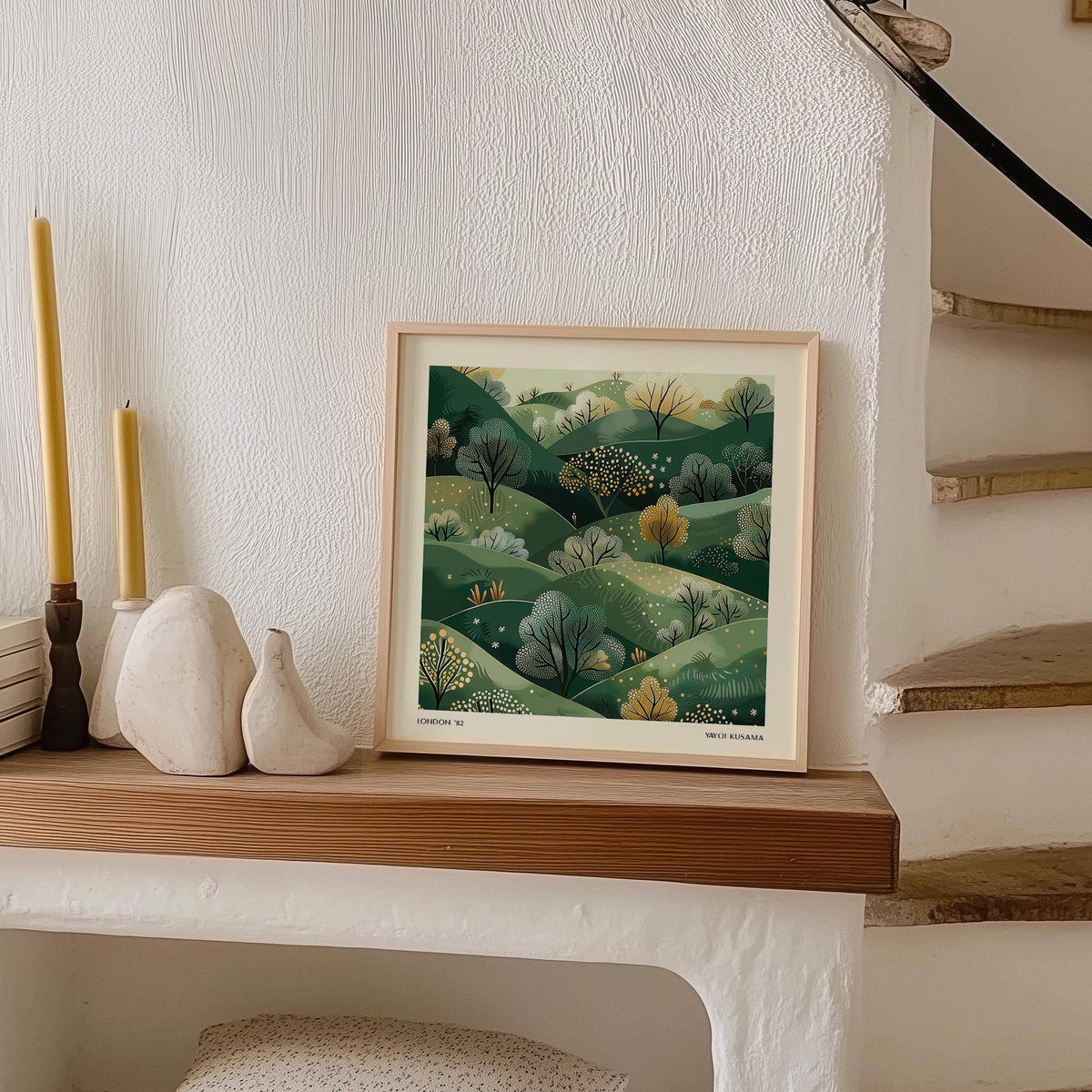 Large nature wall art of green hills with trees in an illustration style leaning on a shelf next to candles