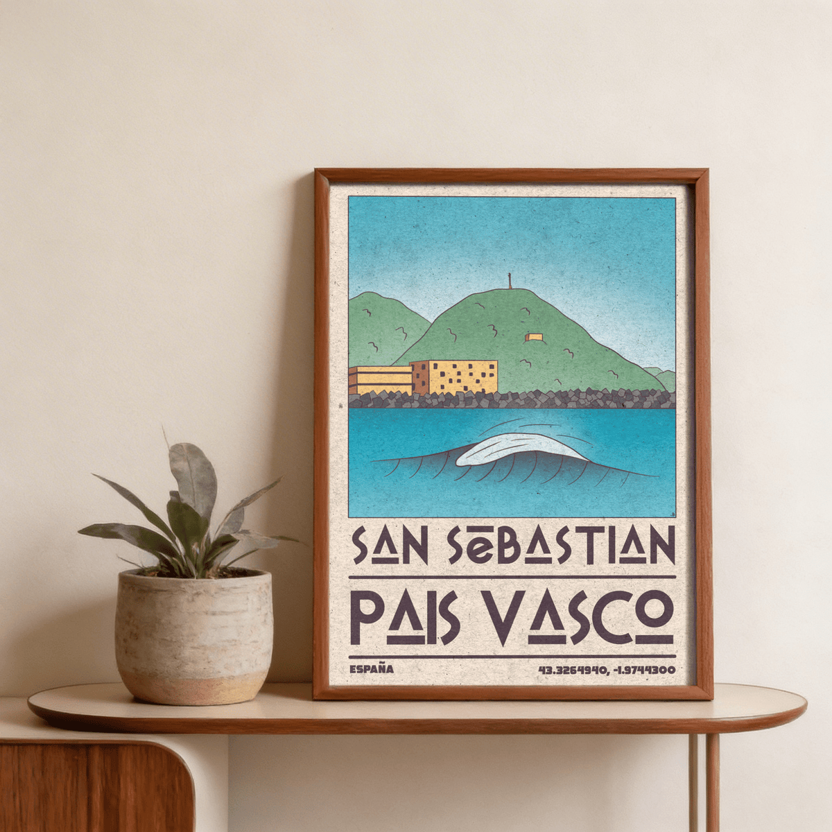Framed Pais Vasco print of a minimalist green hill and blue breaking wave with a plant on table