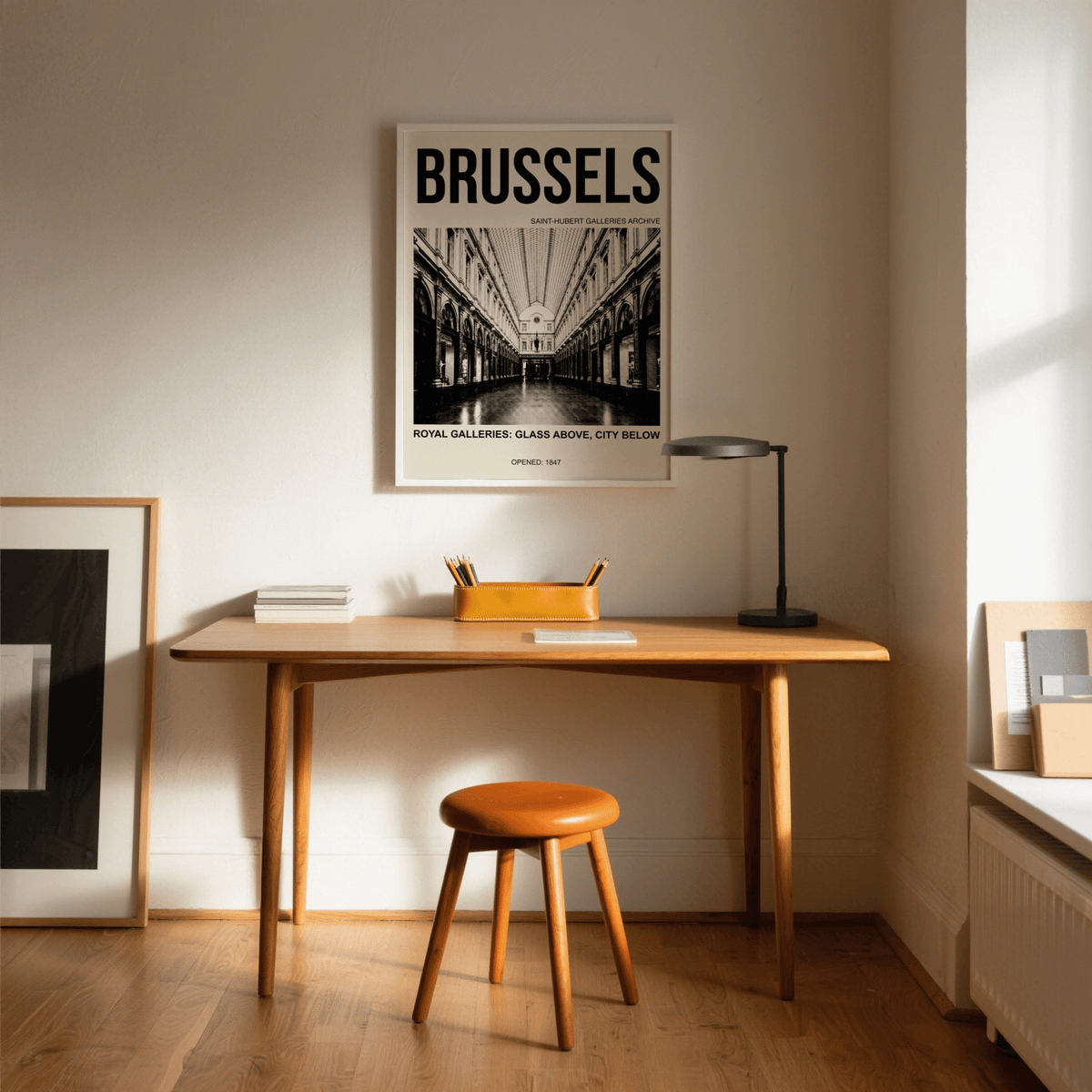 Print on a wall in a room shows Brussels Gallery Print with monochrome photo above a wooden desk and lamp