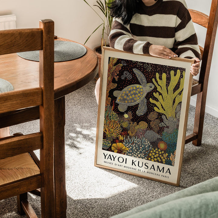 Framed sea turtle wall art held by person in striped jumper showing yellow and orange coral details