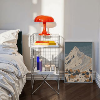 Winter Mountain Art Print leaning on the floor next to a side table with a red lamp and candles in a bedroom