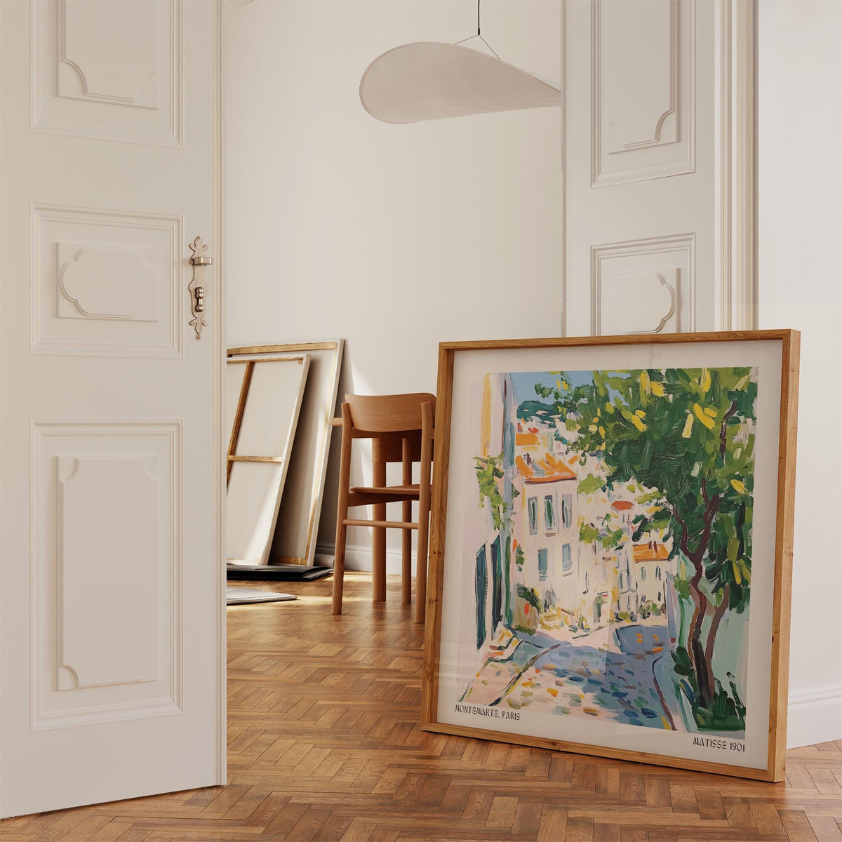 Print leaning on floor of a Paris street with tree in green and orange shades with wooden chair in background