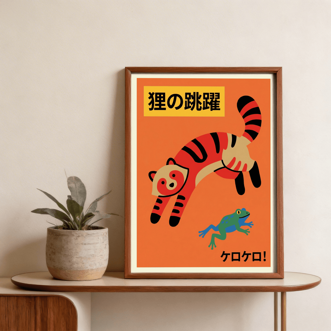 Bright orange Japanese-style poster of a leaping striped raccoon dog and a green frog in a dark wood frame, leaning on a curved oak console beside a potted plant
