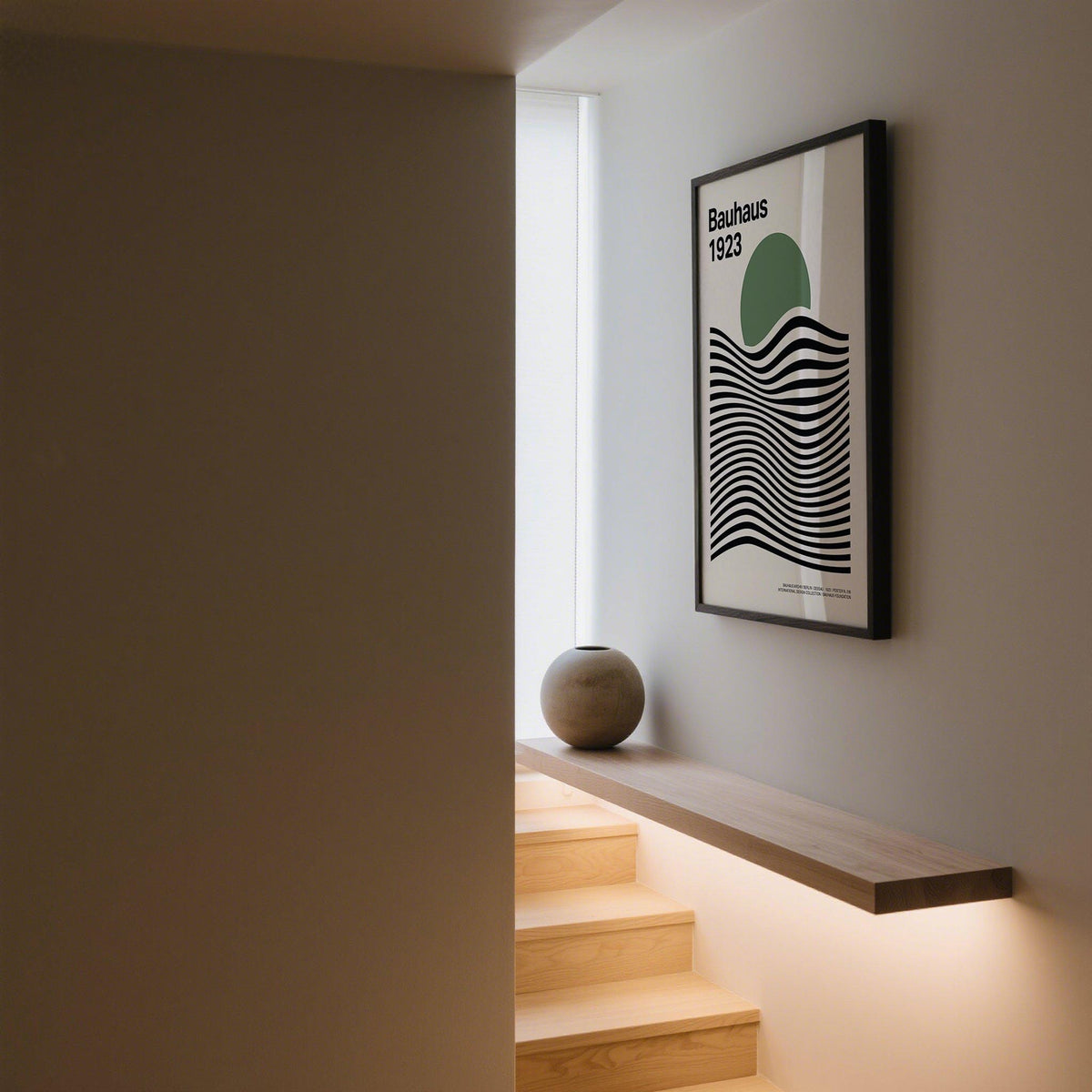 Sage Green Print framed on a grey wall above a wooden shelf with a round stone vase