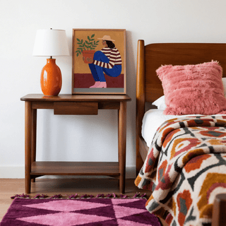 Woman Plant wall art leaning on a bedside table next to an orange lamp in a bedroom