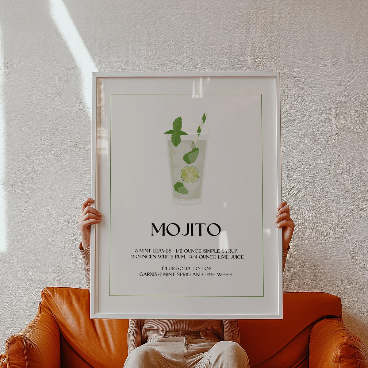 Framed mojito cocktail illustration with green and white details held in hands above a brown leather sofa