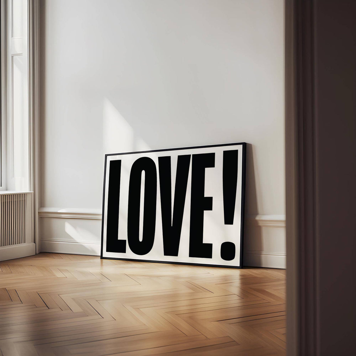 Large motivational posters leaning against wall with LOVE typography in black and white and wooden parquet floor