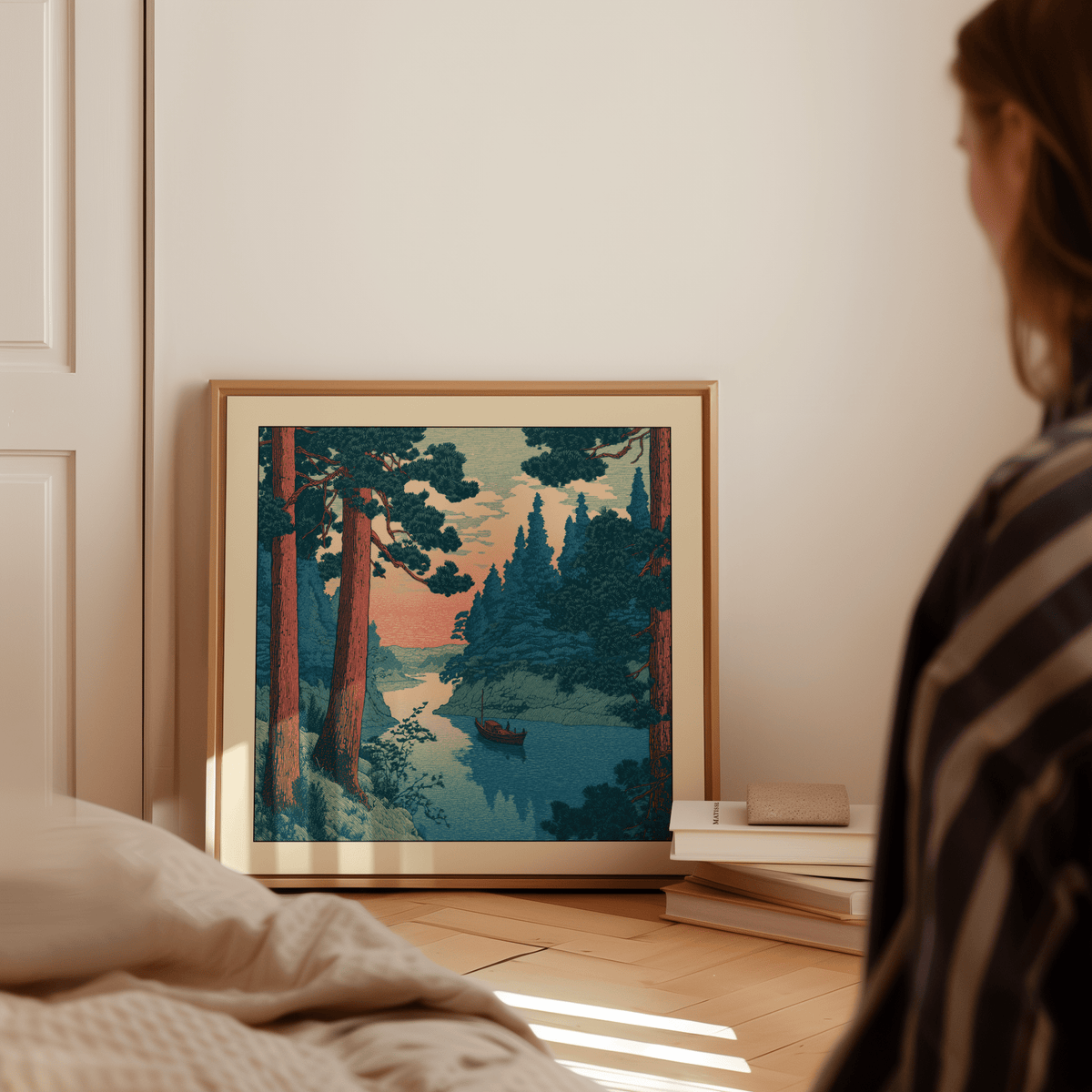 Print leaning on a floor showing a river boat print with pink sky and green trees near books