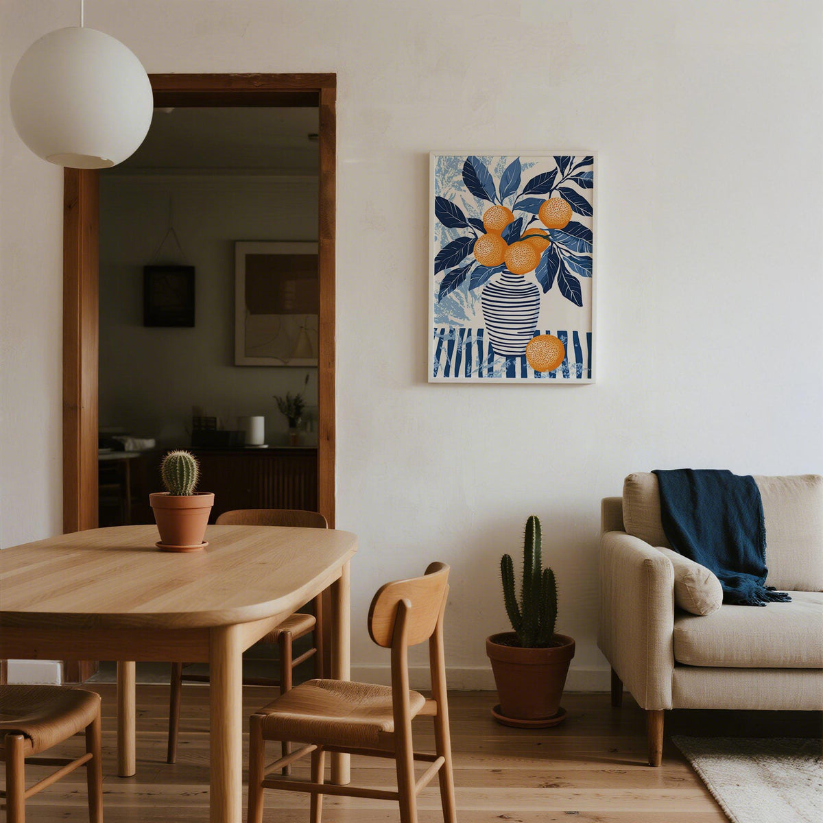 Orange Blue wall art of a vase with oranges and blue leaves above wooden dining table with cactus