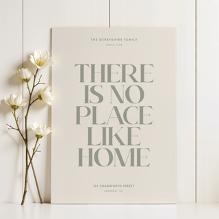 No Place Like Home print in green lettering leaning on a white wall beside white flowers