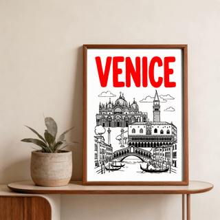 Framed Venice Landmark Art Print in black and red leaning on a wooden shelf beside a potted plant