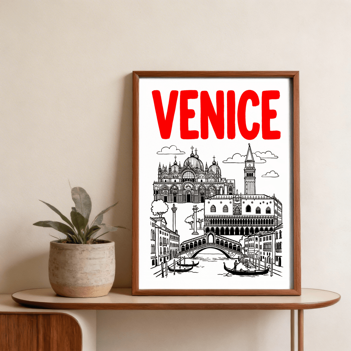 Framed Venice Landmark Art Print in black and red leaning on a wooden shelf beside a potted plant