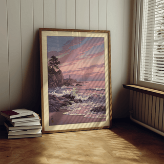 Print leaning on floor of rocky coastline at sunset with soft pink and purple sky near window shutters and books