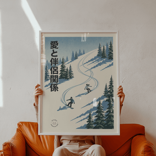 Framed snowboarding wall art with two snowboarders on a snowy slope and pine trees held over an orange armchair