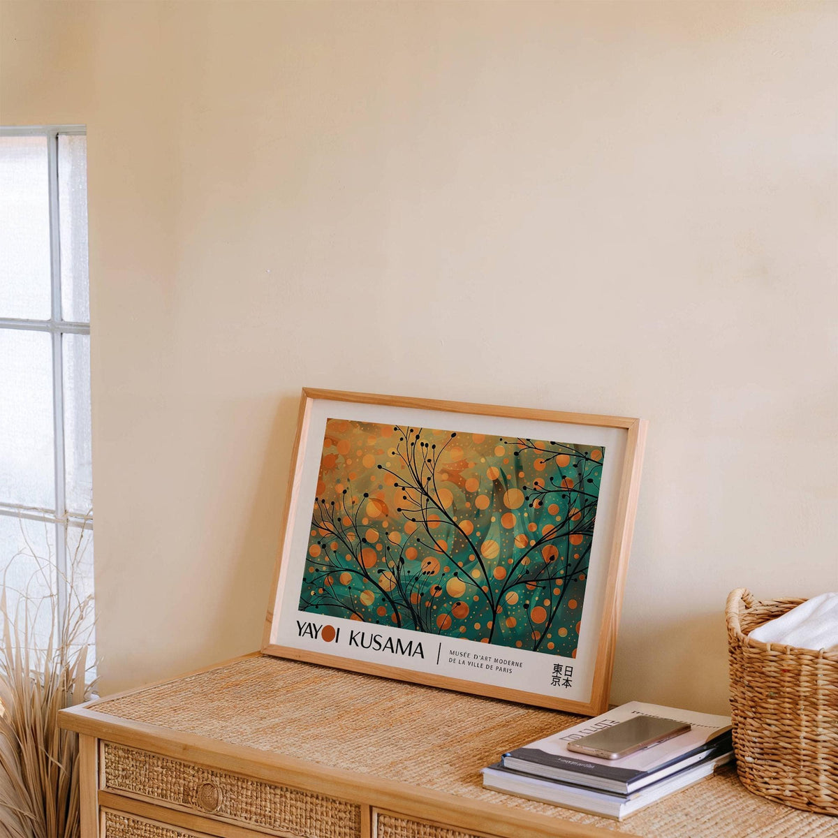 Print leaning on a shelf showing abstract autumn branches with orange and teal dots beside a basket and books