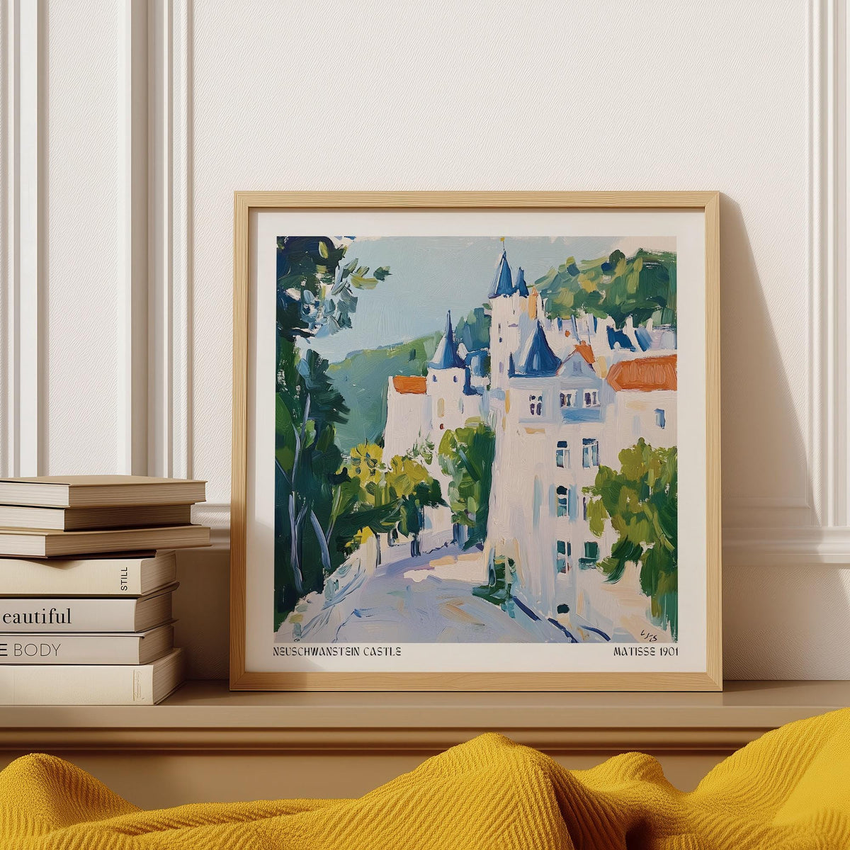 Framed print of medieval castle art in watercolour tones on a mantelpiece beside stacked books and a yellow throw