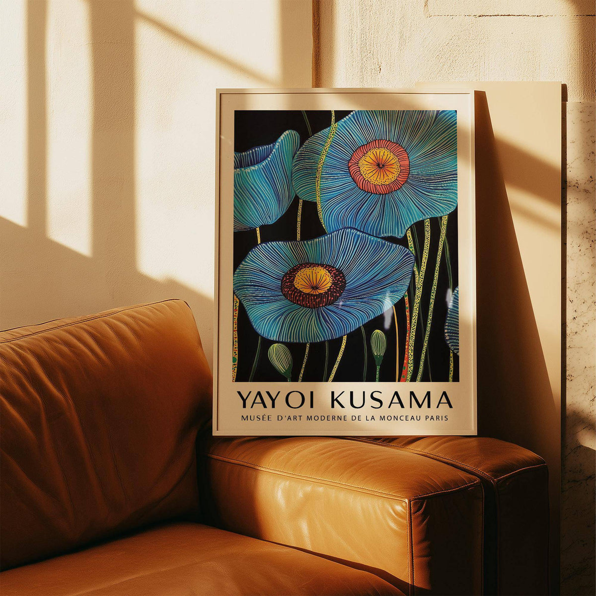 Framed print of Big Flower Wall Art with blue poppy flowers leaning on a tan leather sofa