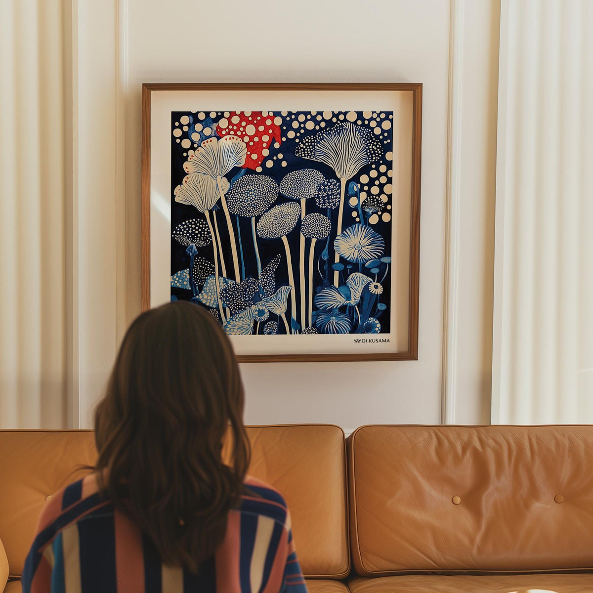 Red and Blue Art framed print of abstract mushroom shapes in red, blue and white above a tan leather sofa