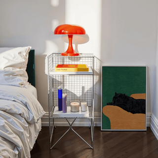 Big Cat Art Print leaning on floor next to a wire bedside table with candles and a red lamp in a bedroom
