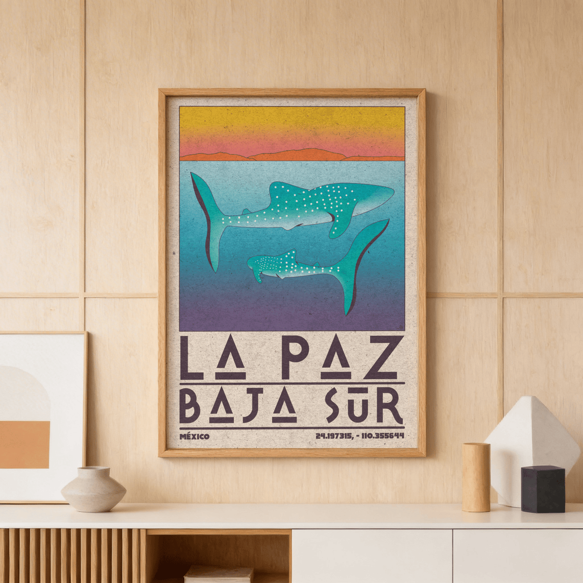 Framed La Paz Mexico poster with blue whale sharks against a gradient sunset on a wood panel wall