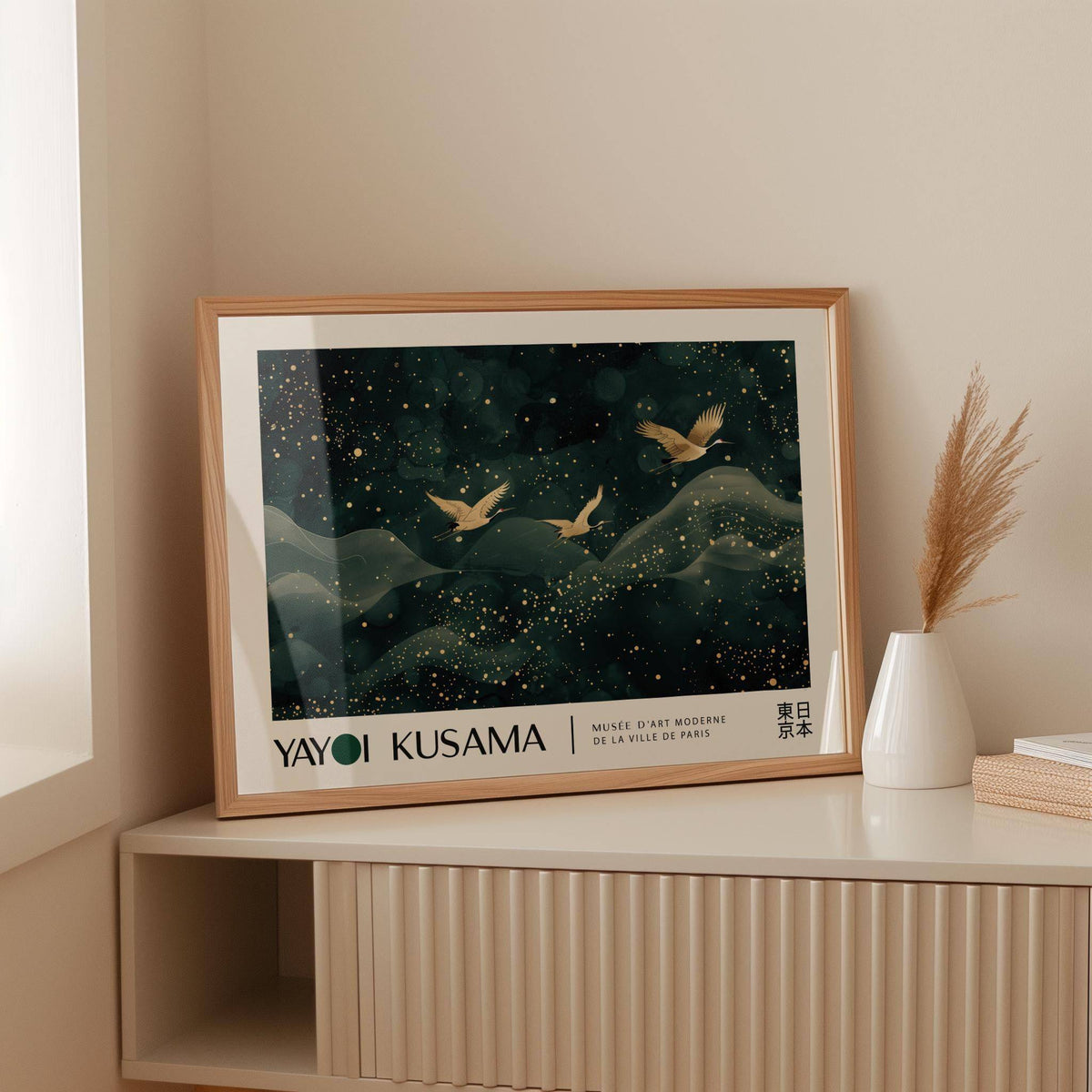 Japanese wall hanging illustrating golden cranes in flight with abstract gold and dark green details leaning on a shelf next to a white vase