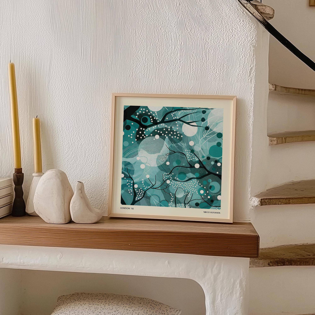 Print leaning on a shelf with abstract moonlit branches in teal and black near candles and ceramic birds