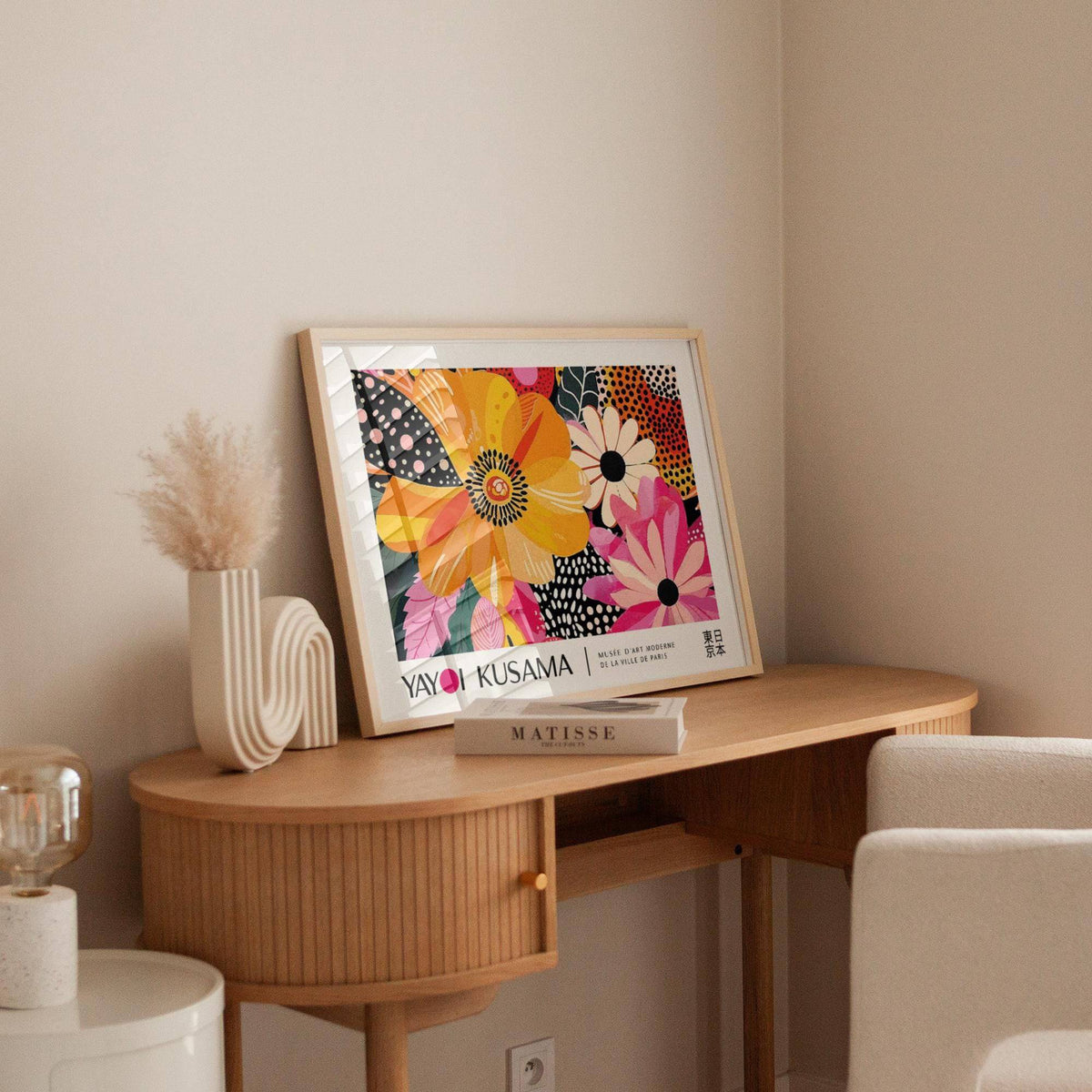Framed Floral Poster Art leaning on wooden desk with cream chair and decorative vase