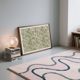 Print leaning on the floor with vintage botanical green and beige floral pattern near a stack of magazines and a lamp