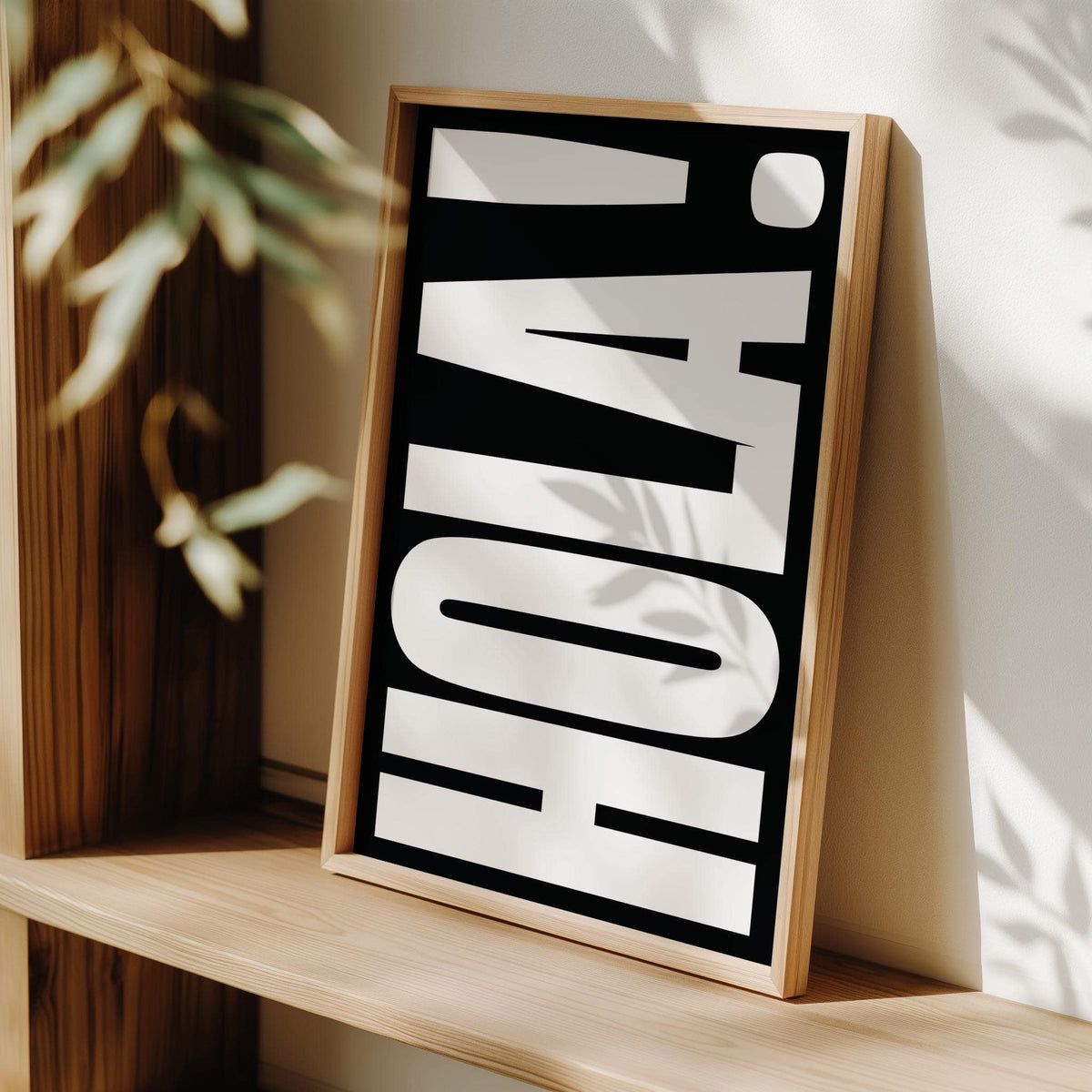 Print leaning on a shelf with bold white HOLA text on black background and plant shadow