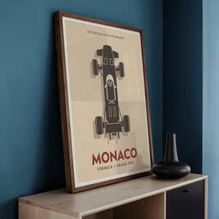 Print leaning on a shelf with a minimalist top-down racing car in brown and beige and a black vase nearby