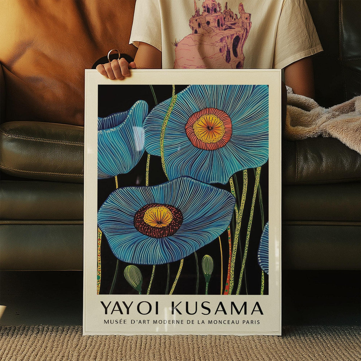 Framed Big Flower wall art of blue poppy flowers with yellow centres held up in front of a leather sofa