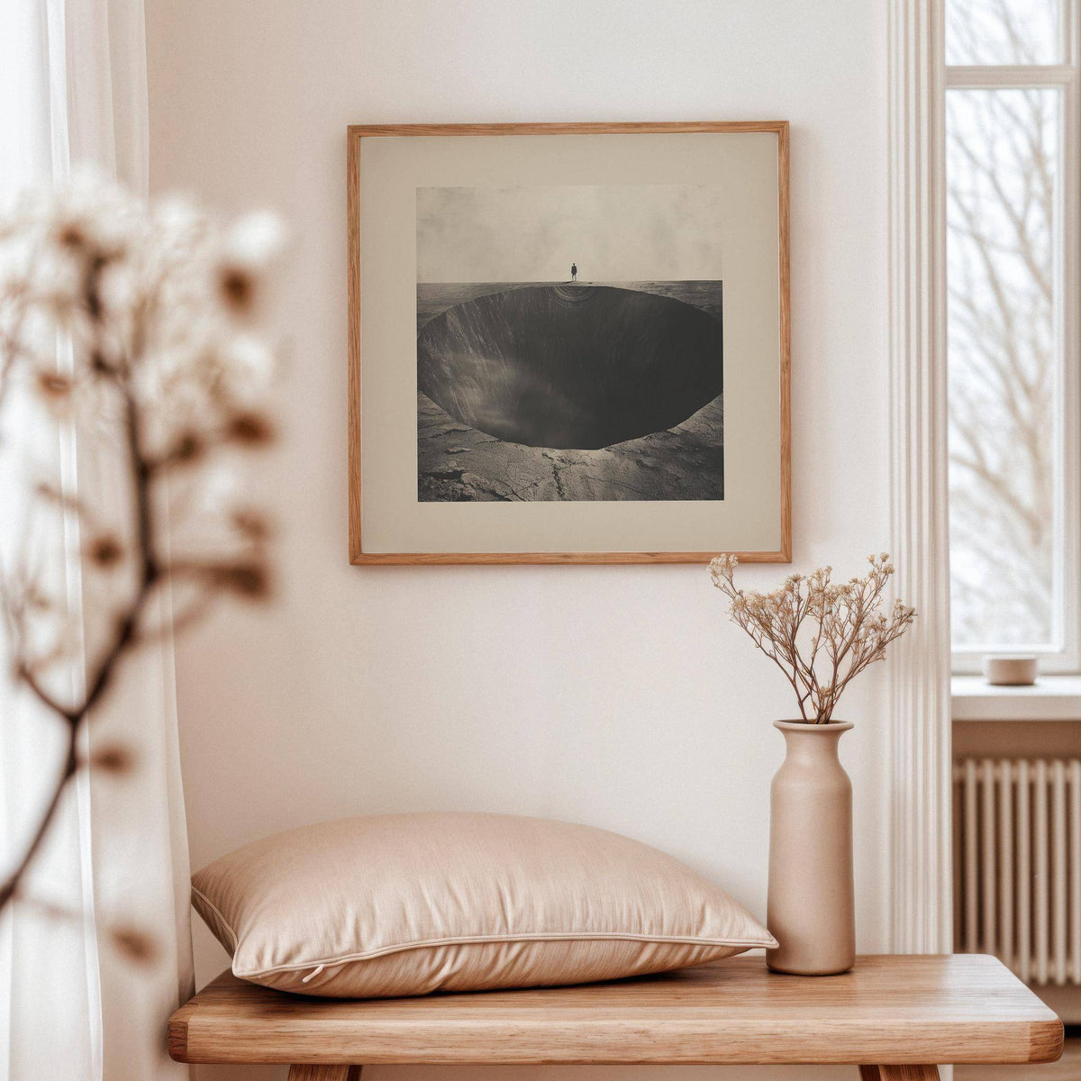 Surrealist wall art of a vast abyss hole in muted tones above a wooden bench with cushion in a bright room