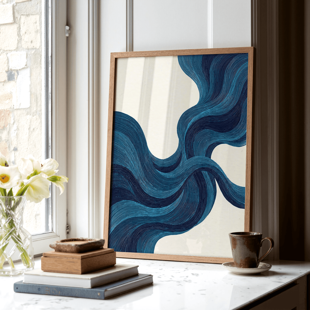 Blue Line wall art leaning on a windowsill with a stack of books and a cup nearby in natural light