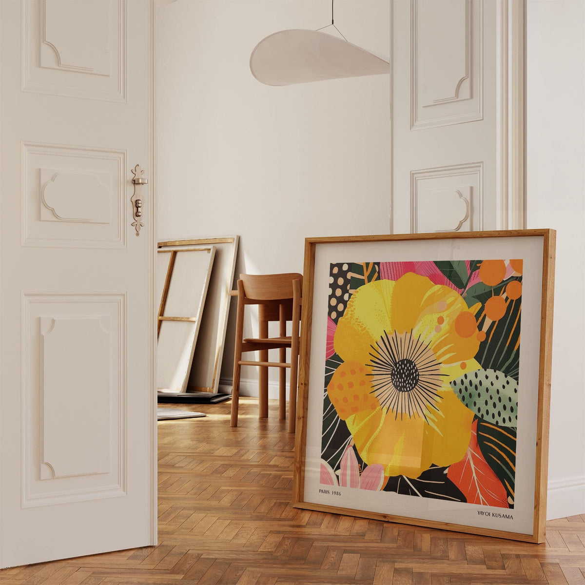 Print leaning on floor of a yellow flower with pink and green leaves in a hall with wooden chair