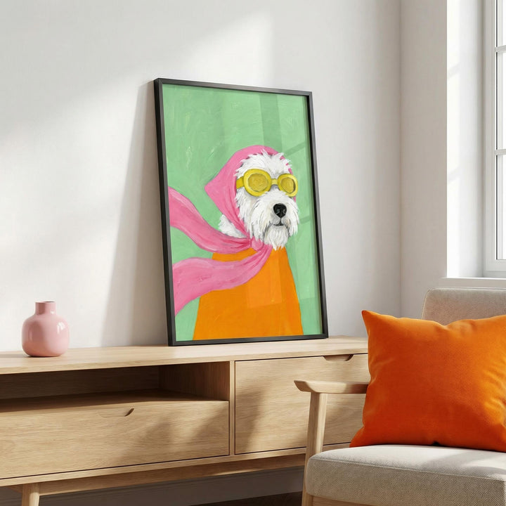 Print leaning on a shelf of a dog with yellow aviator goggles and a pink scarf alongside a pink vase