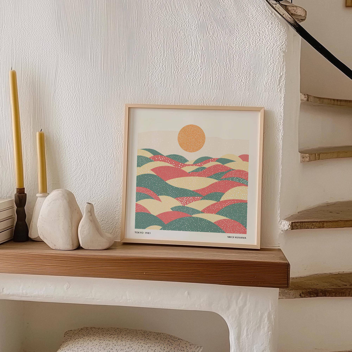 Pastel abstract artwork of dotted hills and sun leaning on a wooden shelf with candles