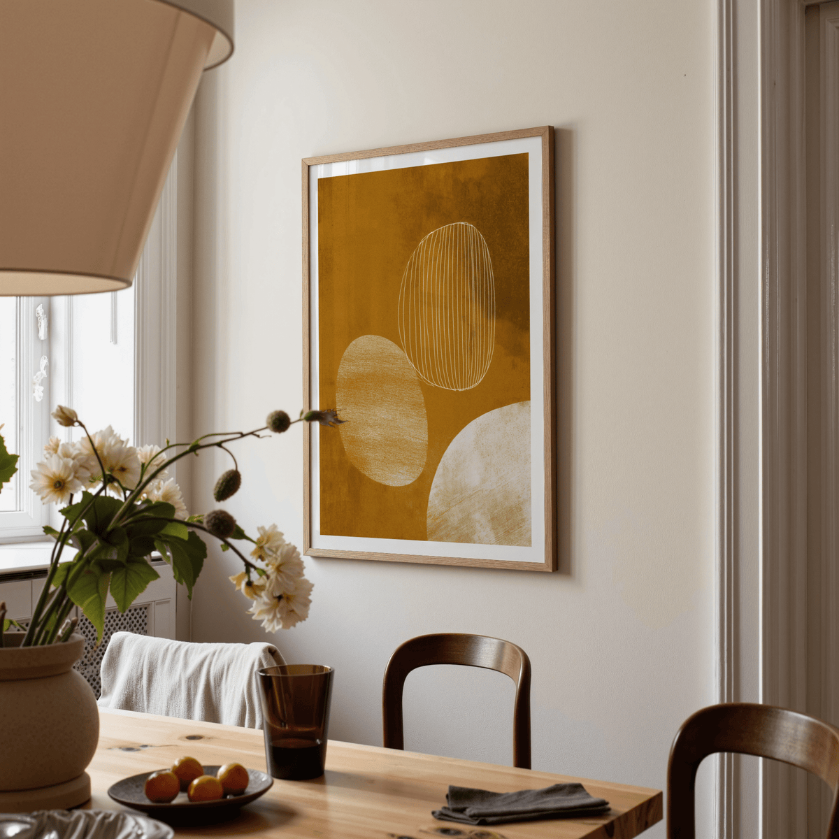Minimalist line art poster with abstract organic shapes in ochre and cream on a wall above a dining table