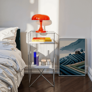 Print leaning on the floor of mountain tea plantation illustration beside a nightstand with candles and a red lamp