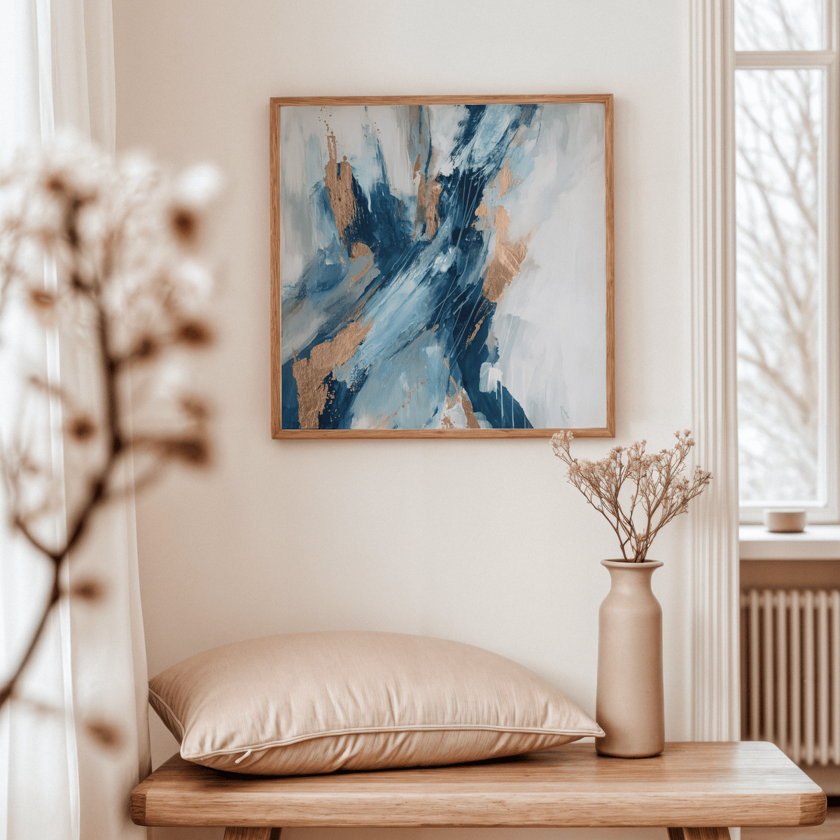 Blue abstract wall art with blue and gold splashes above a wooden table with pillow and vase