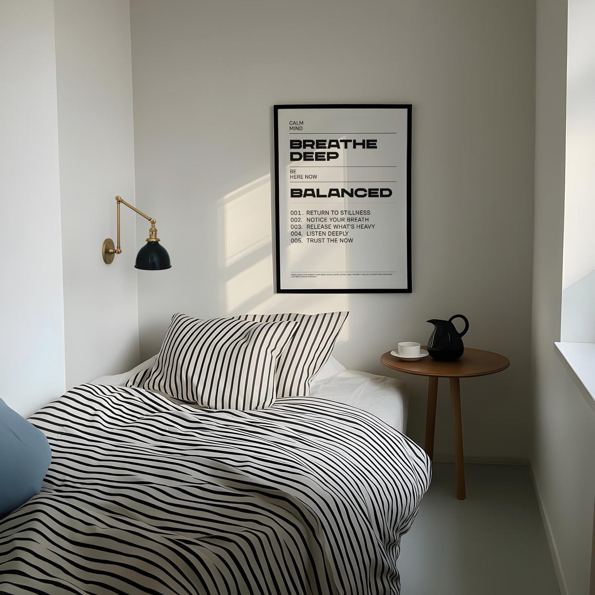 Zen Quotes Breath wall art with black text in a black frame above a bed with striped bedding and a small wooden side table