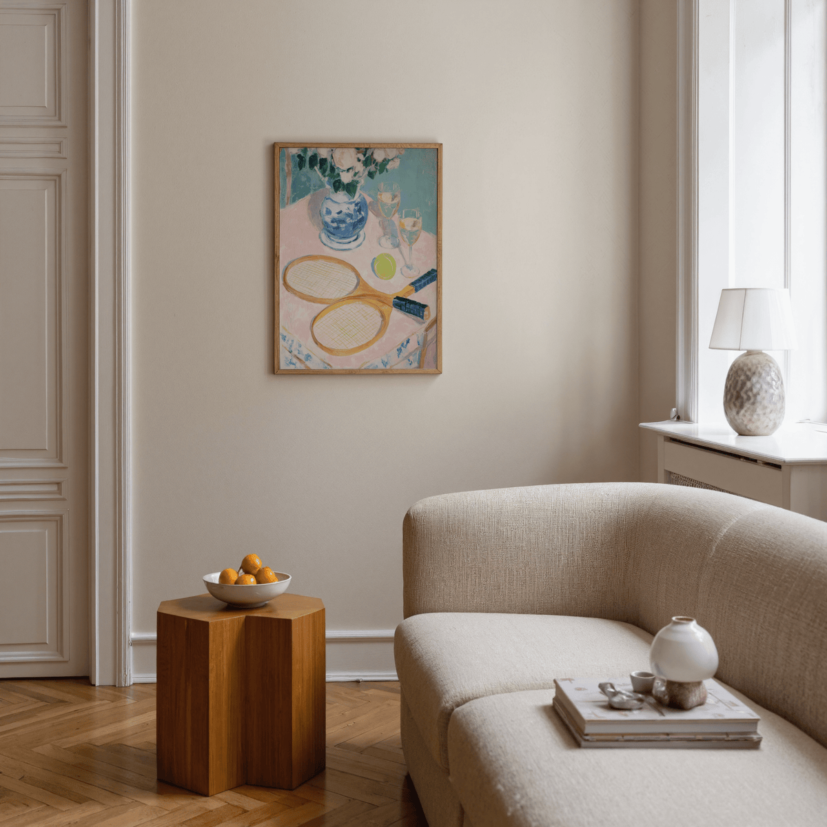 Tennis Still Life Print hung on a beige wall above a wooden side table with a bowl of fruit in a living room