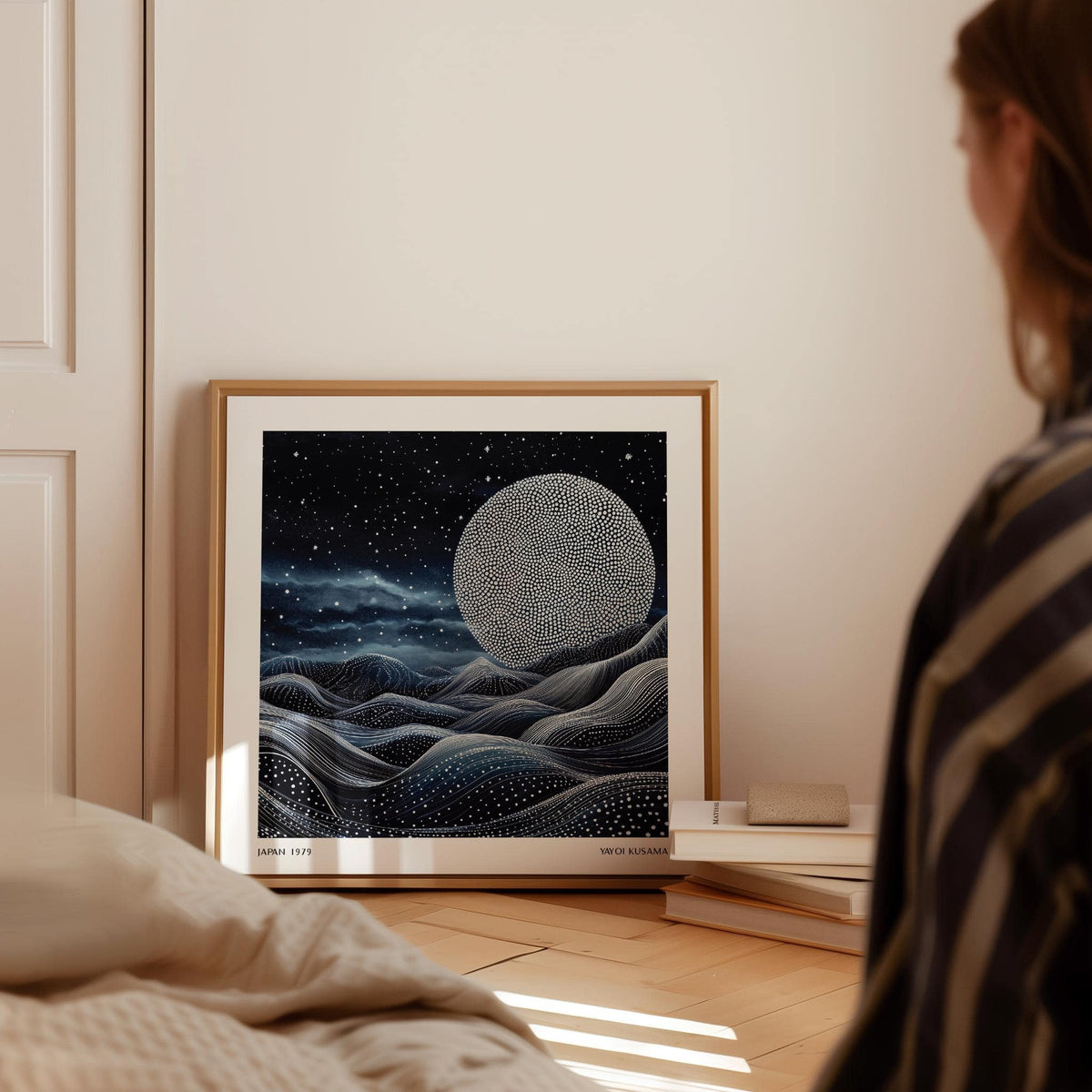 Unique wall art for bedroom leaning on a wooden floor with books beside it and a large moon with dotted pattern