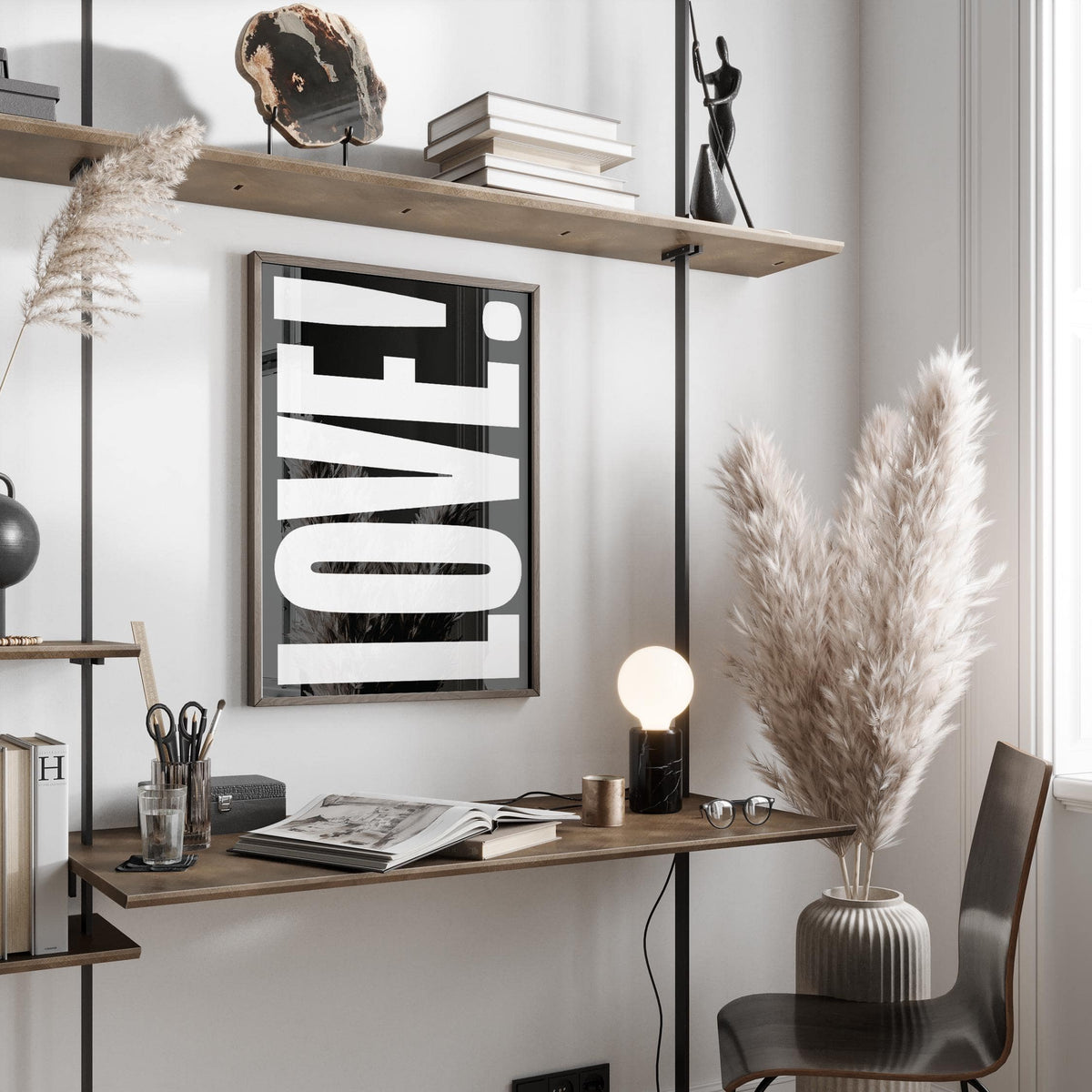 Print on a wall of LOVE typography in white on black above a wooden desk with lamp and pampas grass