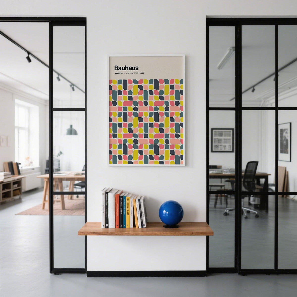 Colorful wall poster of Bauhaus geometric pattern in blue yellow and pink above a wooden shelf with books and a blue ball